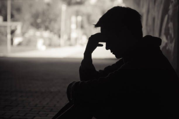 Young man in silhouette sitting in emotional distress on a dark street