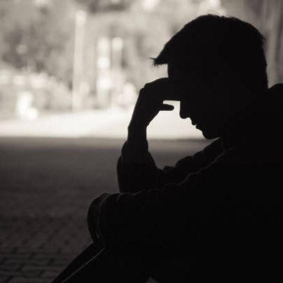 Young man in silhouette sitting in emotional distress on a dark street